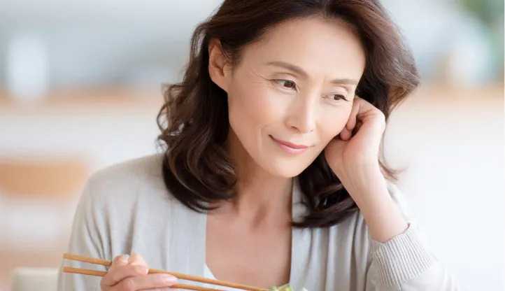 食事中に頬へ手を当て、噛みにくさを感じている女性