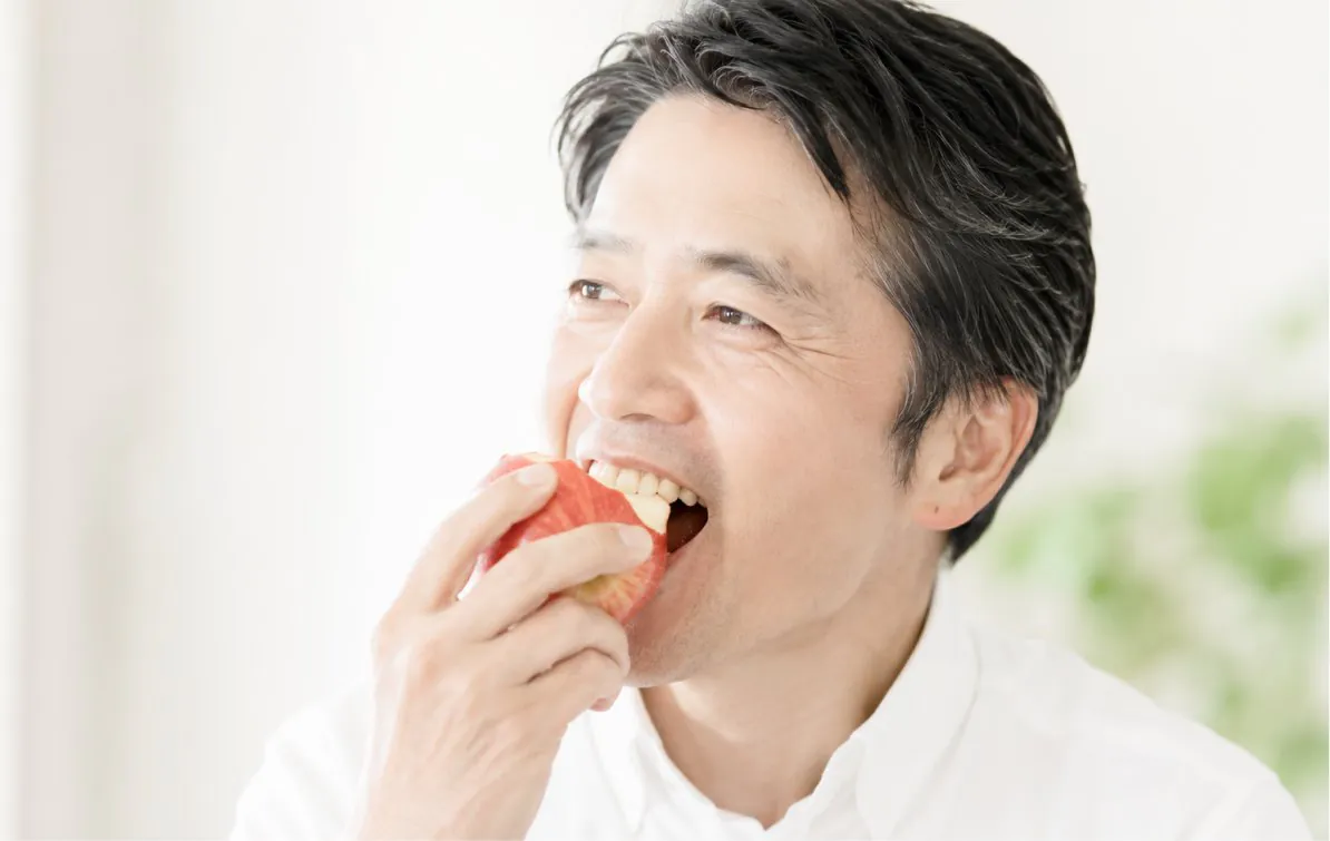 りんごをかじる男性。インプラントで自分の歯のようにしっかり噛めている様子。